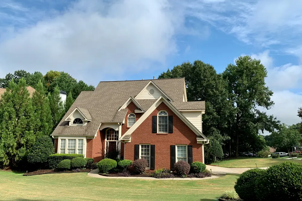 A large brick two-story rental home with a manicured lawn and mature landscaping