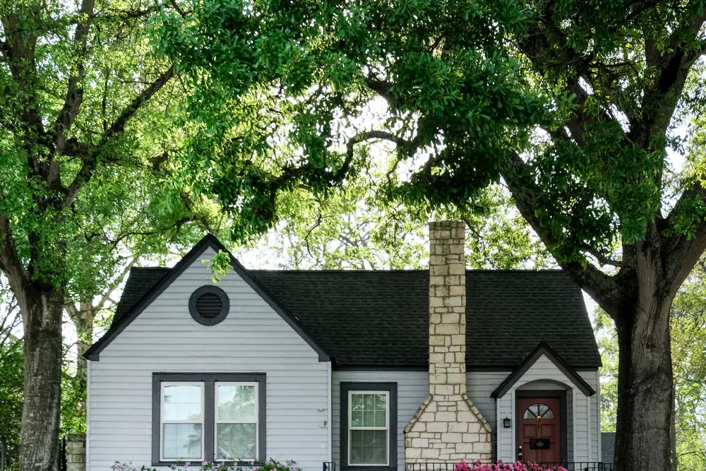 A small white cottage-style Columbus home framed by mature trees and flowering shrubs