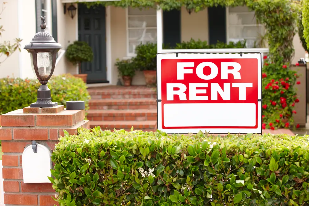 A For Rent sign in the front garden of a single-family home with a covered porch